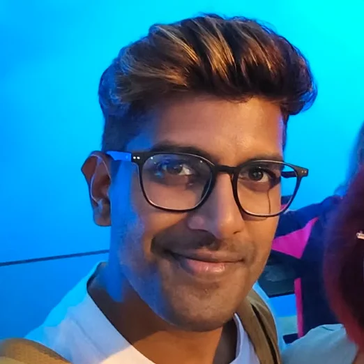Tirish smiling, in glasses, with a river lit blue behind him